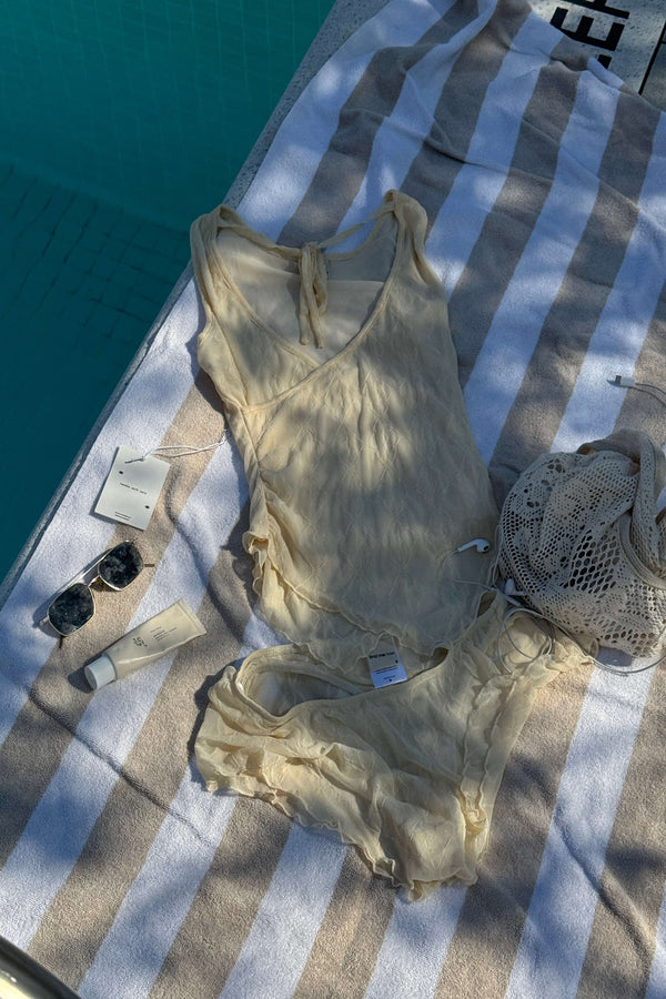 Beige lace tank top and shorts on a striped towel by a pool with a lace thong